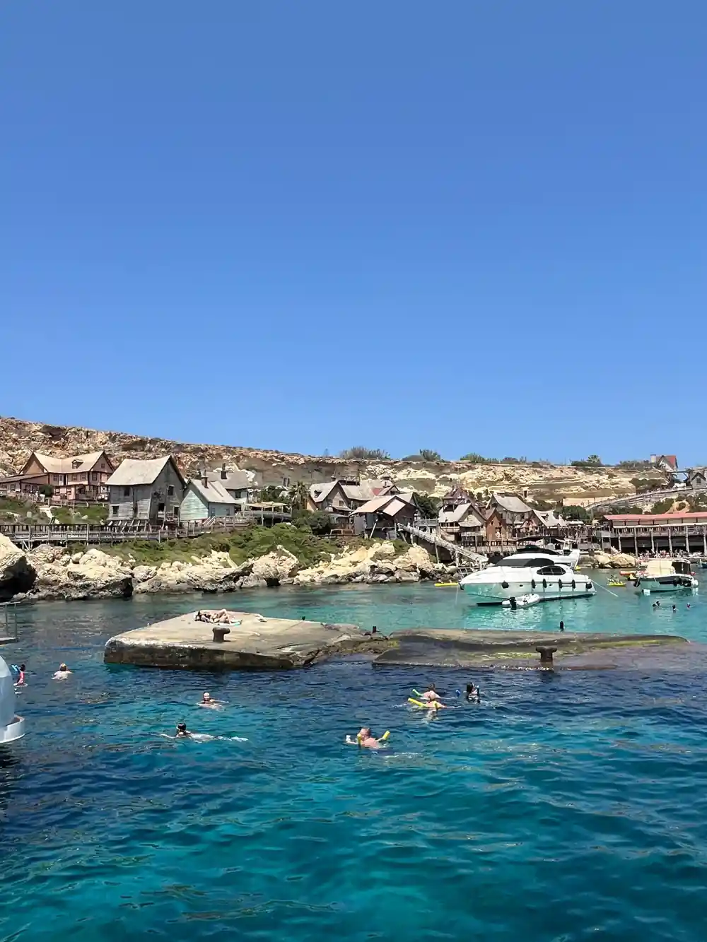 Anchor Bay with the wooden village behind and swimmers in the inlet