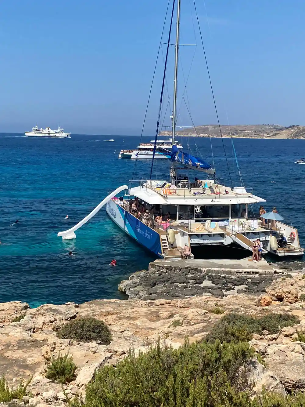 The blue catamaran anchored off a rock shelf, swimmers in the water