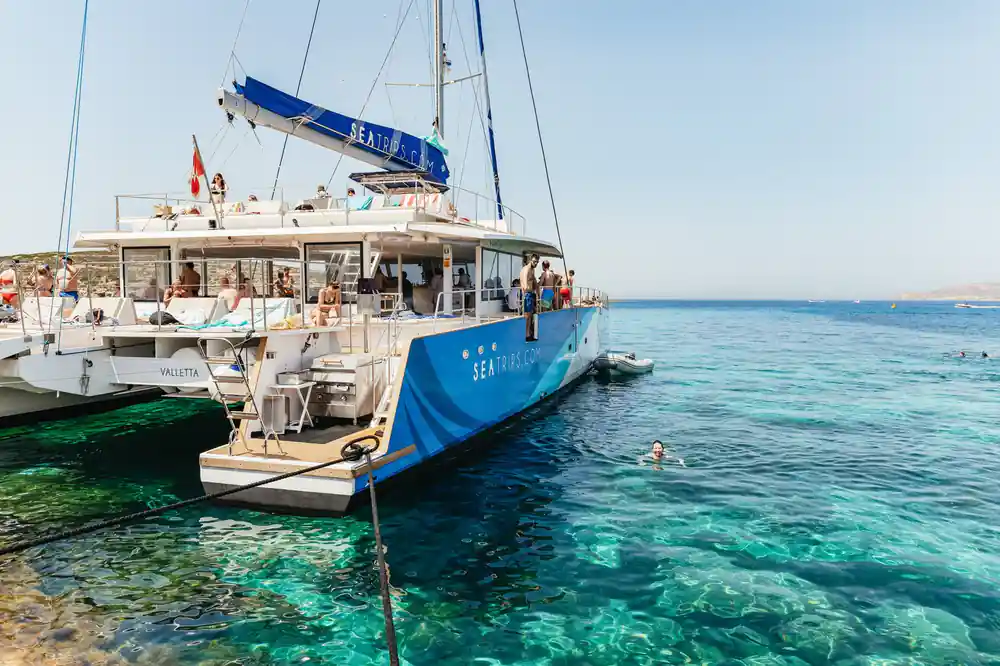 The catamaran at anchor in glassy water beside a low rock shelf