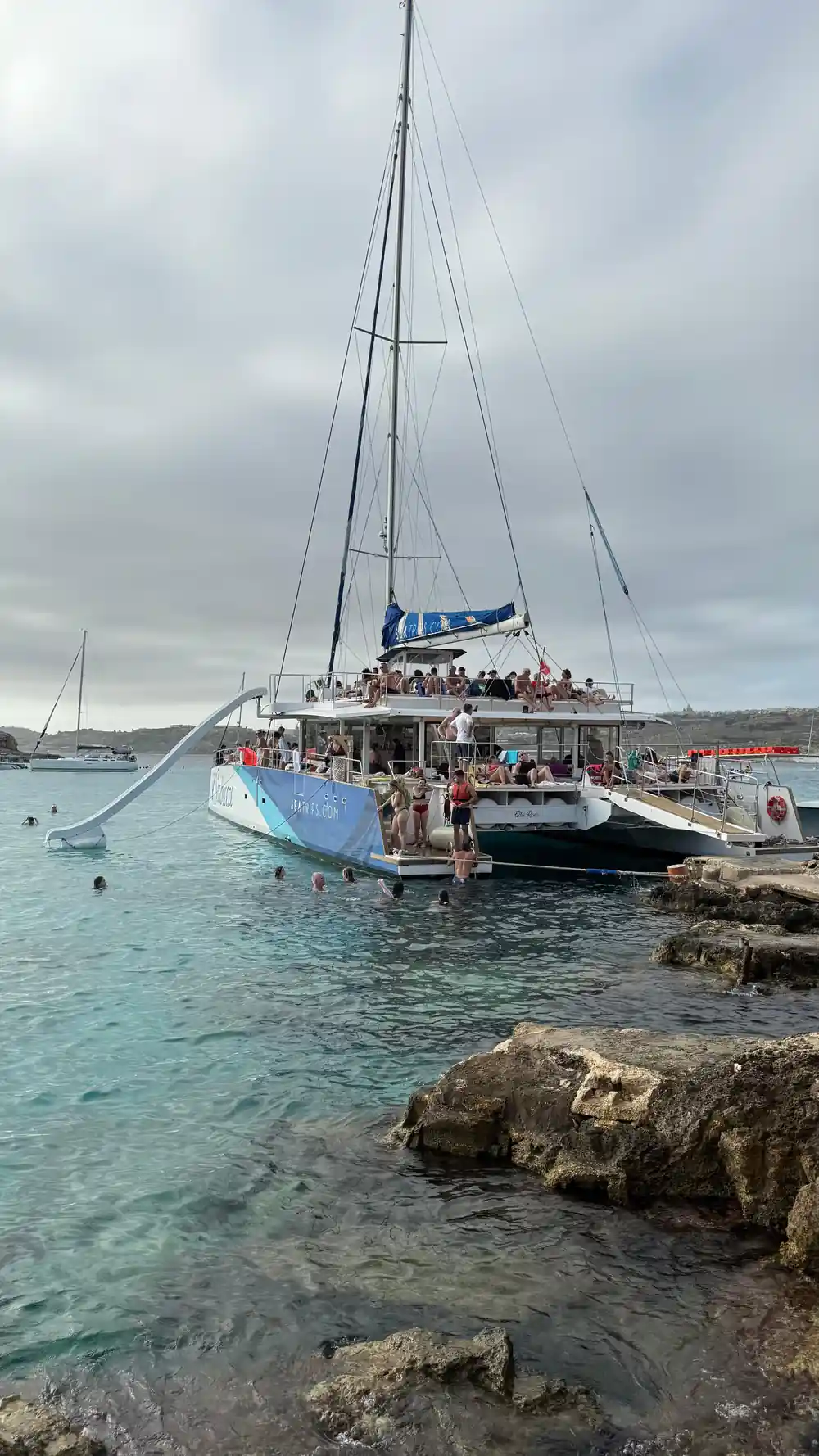 A catamaran anchored off the rocks with a slide down to the water