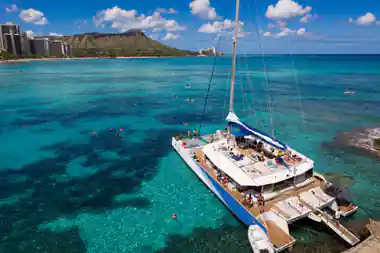 The catamaran seen from above, full deck, anchored over pale turquoise water