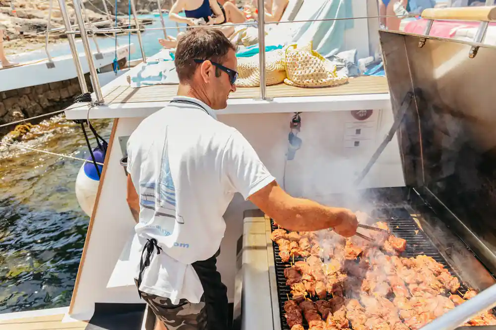 A crew member turning kebabs over the grill on deck