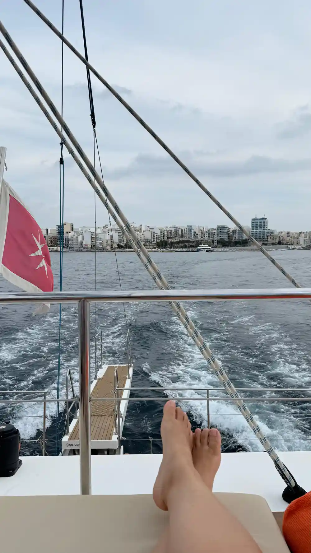 A Maltese flag at the stern with the city shore in the distance