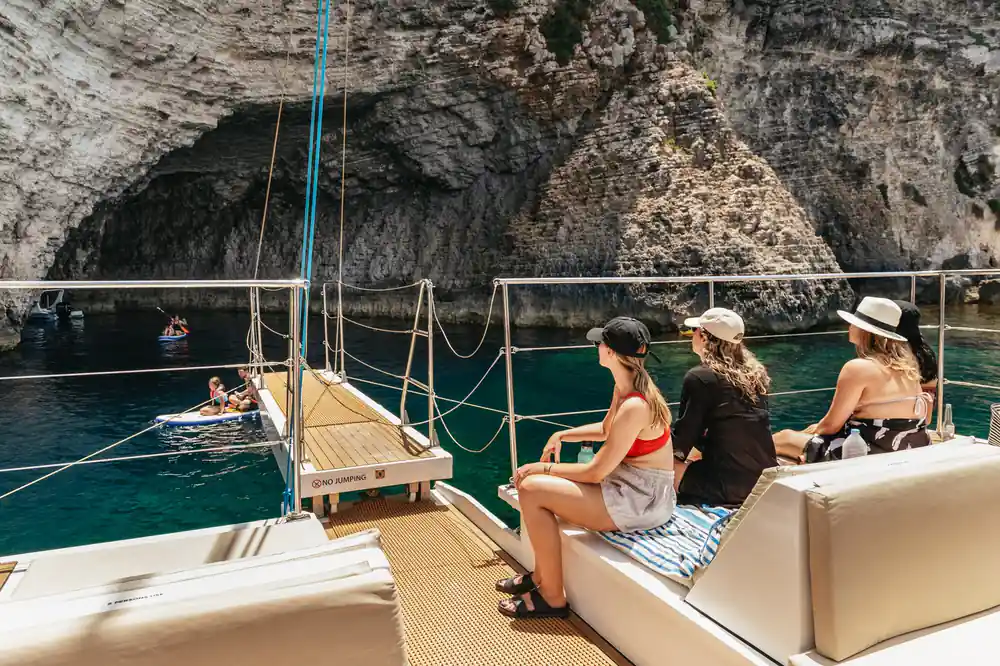 Passengers sitting on the side deck under a high limestone cliff