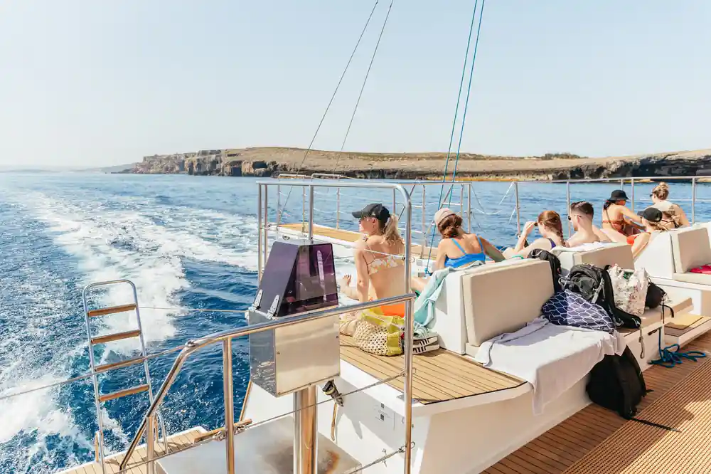 Passengers on sun beds along the deck as the boat runs past a low coast