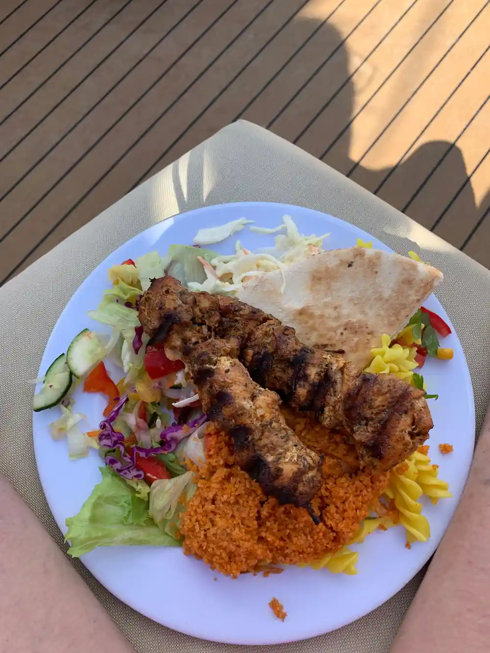 A plate of grilled kebabs with salad, rice and flatbread on deck