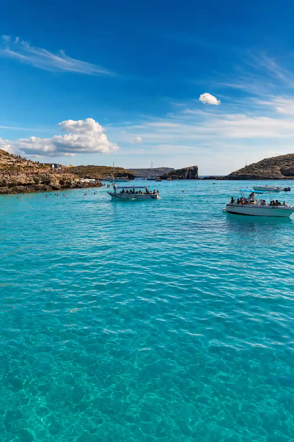 Small boats scattered across the bright blue channel off Comino