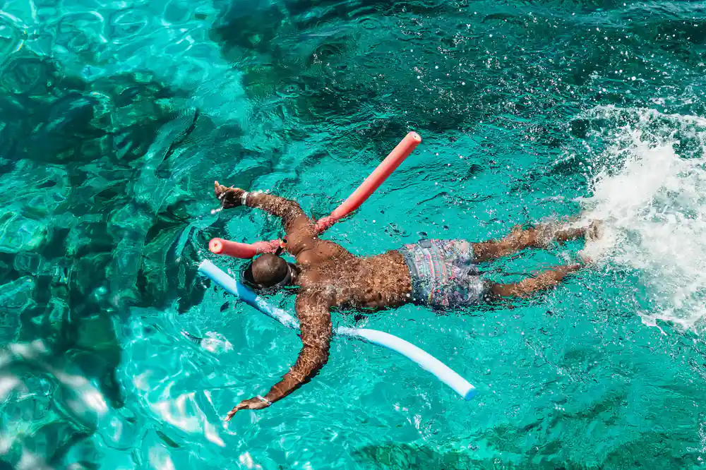 A snorkeller with a pool noodle floating over bright blue water