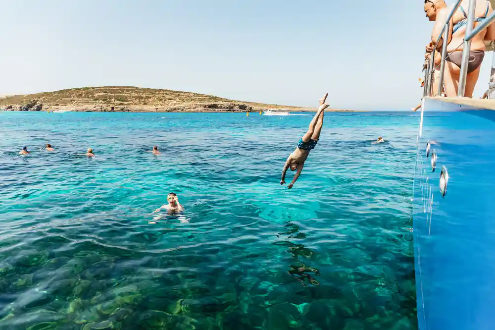 A swimmer diving from a rock into clear turquoise water