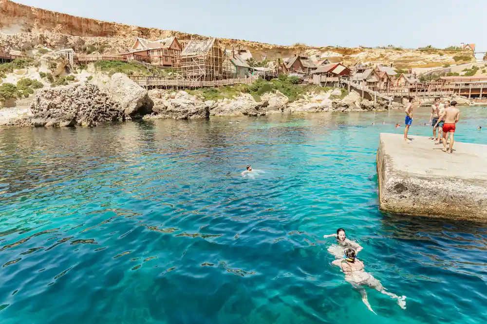 Swimmers in clear water below a low green shoreline