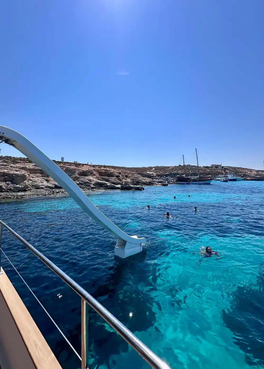 Swimmers in the water beside the boat below a low rocky shore