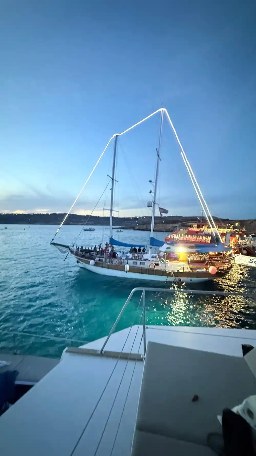 A traditional wooden sailing boat anchored off a low coast