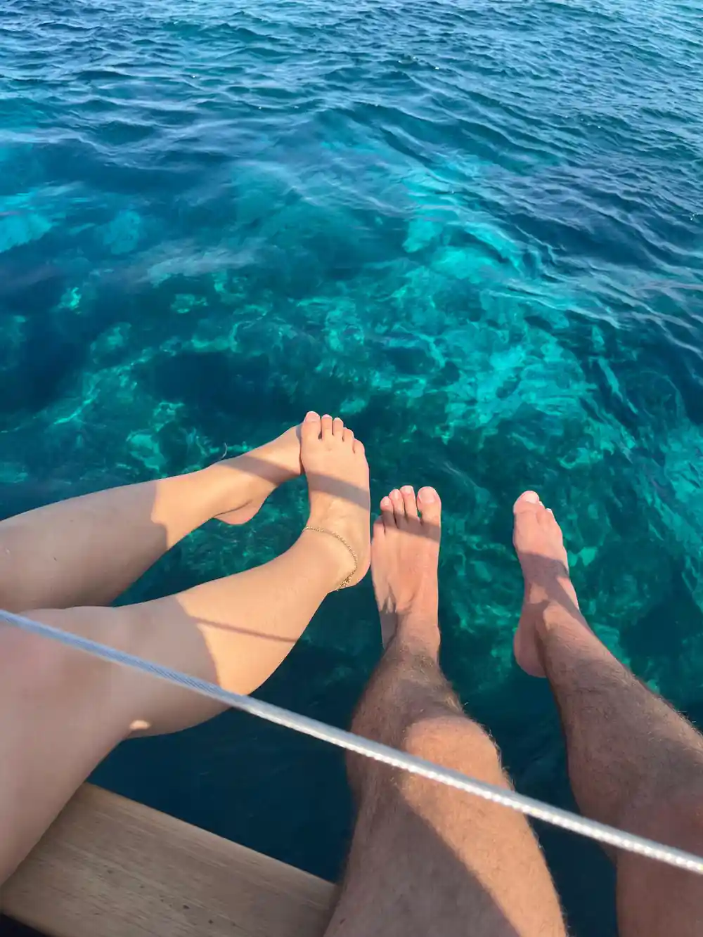 Two pairs of feet over the rail above bright moving water