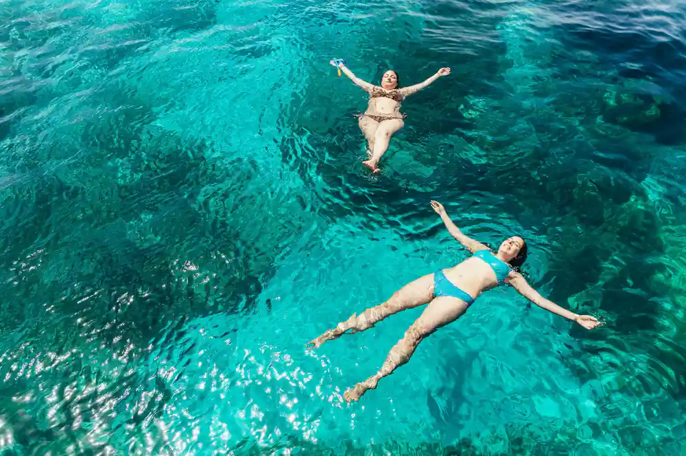 Two swimmers floating on their backs in bright shallow water