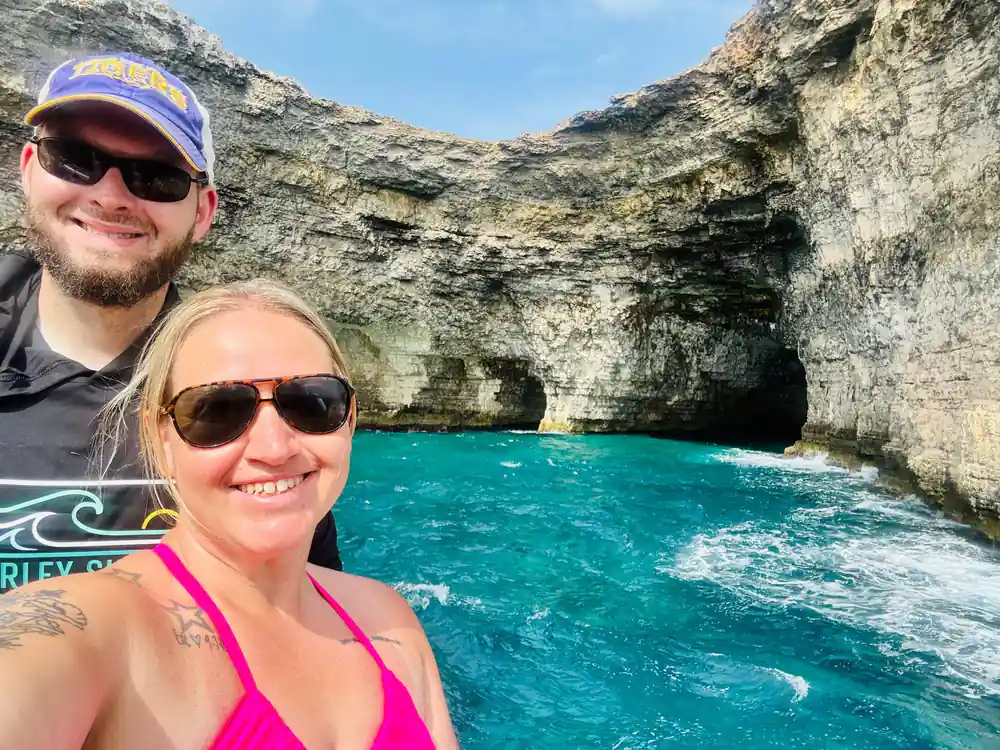 Two swimmers in the water at the foot of a cave-pocked cliff