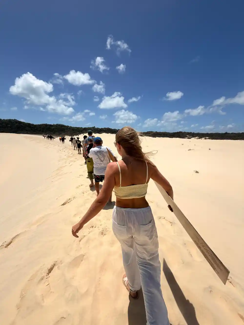A woman walking along a sandy beach towards a group at the water