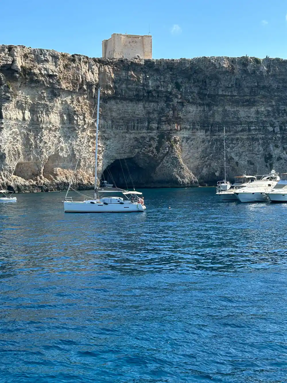 Yachts at anchor under a high cliff face with a cave at its base